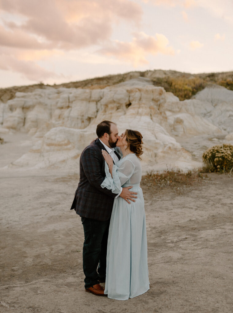 A couple kisses at their engagement photos at the Paint Mines Interpretive Park near Colorado Springs, Colorado. Find out what to wear for your destination engagement photos.