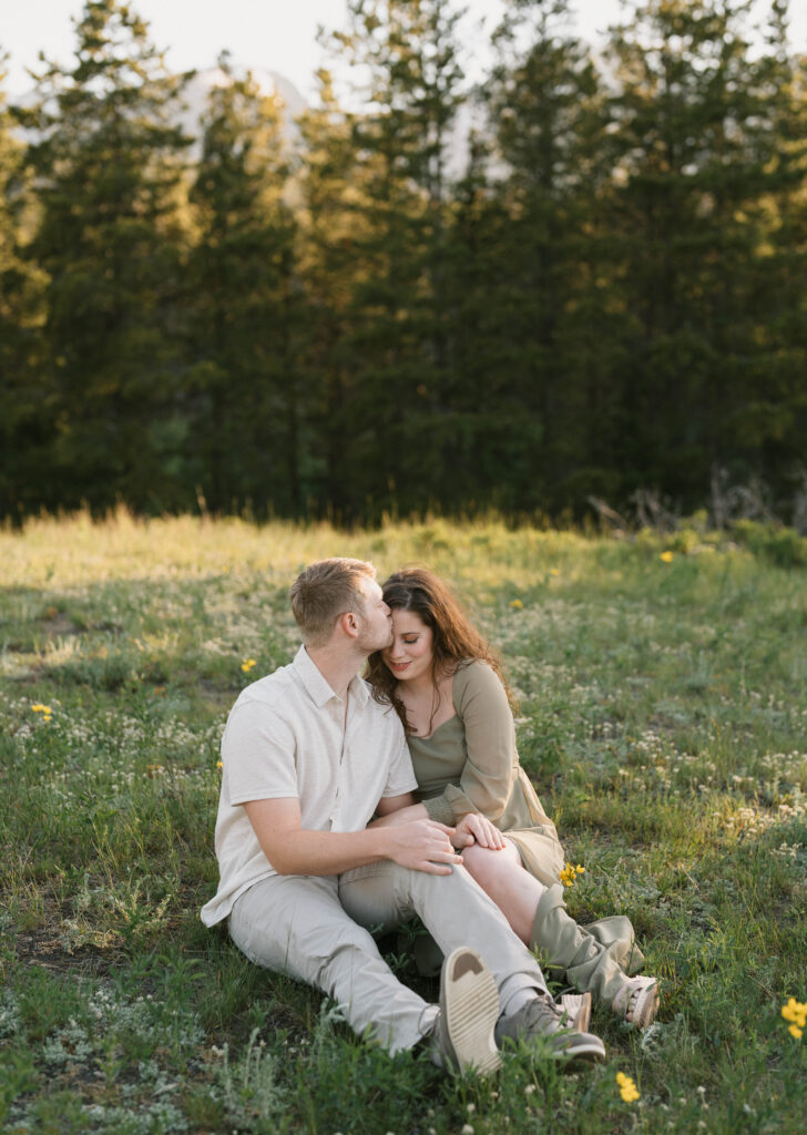 A couple sits at Sprague Lake for their engagement photos in Estes Park. Learn how to choose the perfect outfit for engagement photos in Colorado.