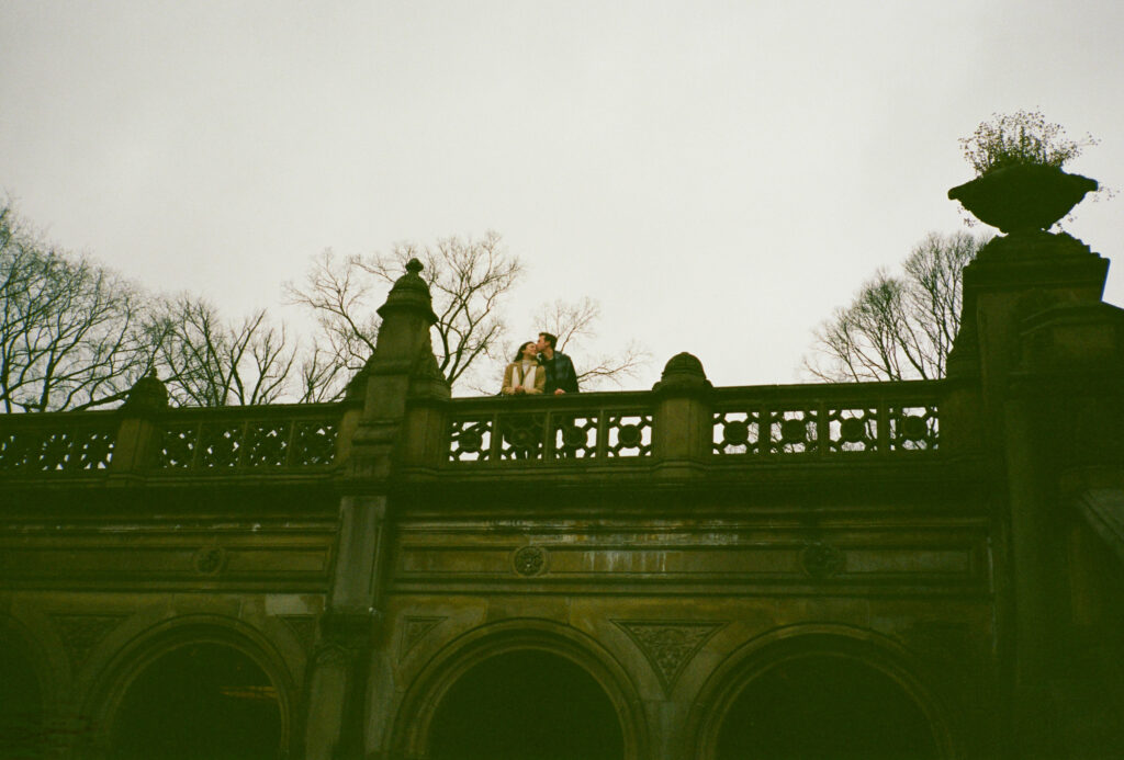 A stands sits together at Bethesda Terrace in Central Park. Discover documentary film photos from an engagement session in New York City captured on 35mm film.  