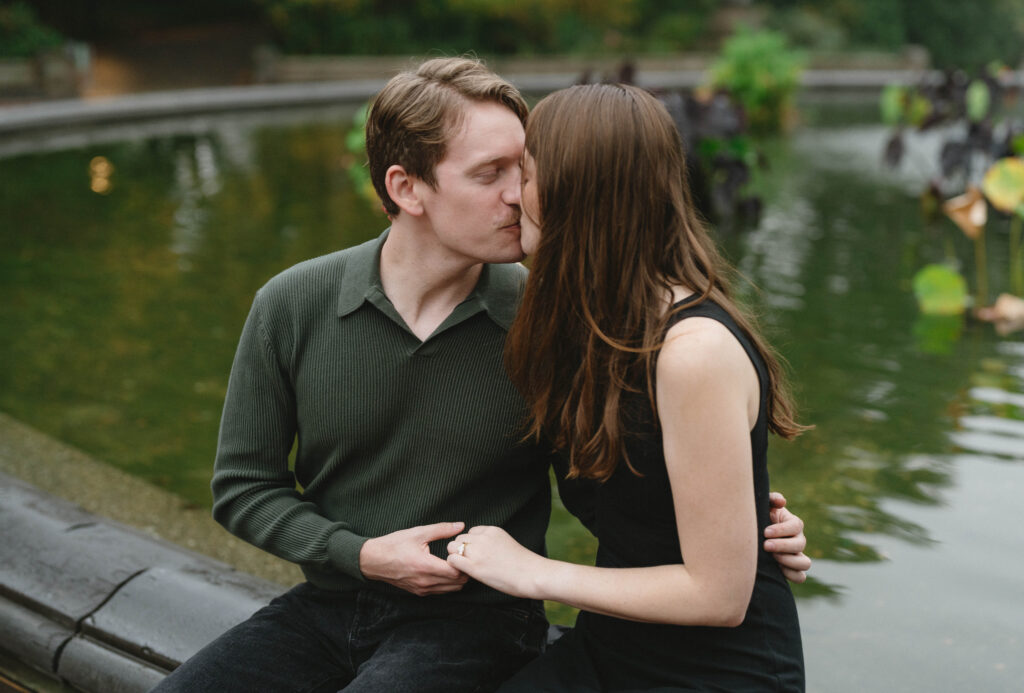 A couple kisses while sitting at Bethesda Fountain inside Central Park in NYC, showcasing the intimate feeling that New York City and Manhattan gives your engagement photos. 