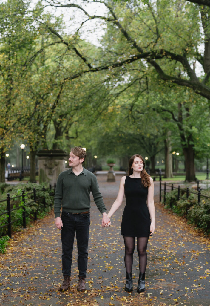 A posed photograph of a couple standing together inside Central Park near Bethesda Terrace in the fall with autumn colors, showcasing the intimate feeling of New York City and how it's perfect for engagement photos.