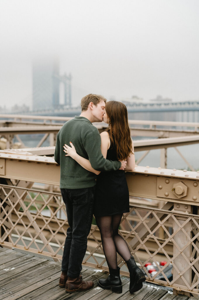 A candid photo of a couple kissing on the iconic Brooklyn Bridge near Manhattan and Brooklyn in NYC for their engagement photo session. 