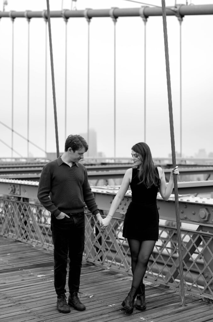 An engaged couple poses the iconic Brooklyn Bridge in the early morning light, showcasing the unique essence of their engagement photo session in New York City.