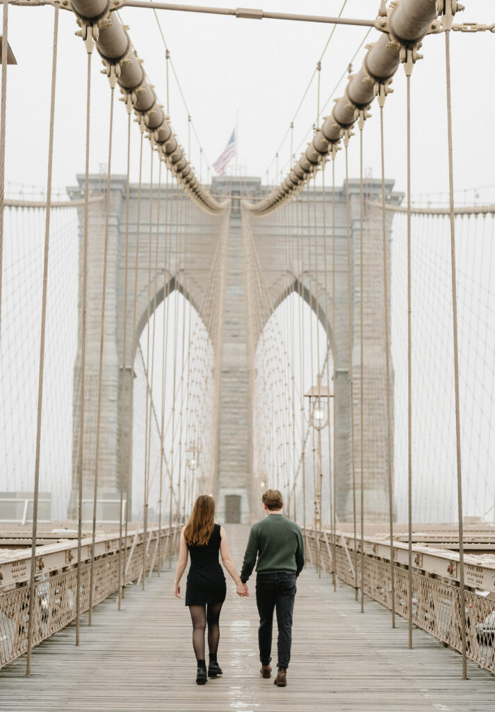 A loving couple captured during a charming stroll across the iconic Brooklyn Bridge in the early morning light, showcasing the unique essence of their engagement photo session in New York City.