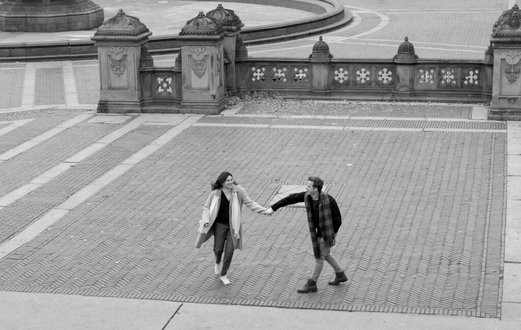 A couple embraces at Bethesda Fountain in Central Park. Discover candid photos from an engagement session in New York City.