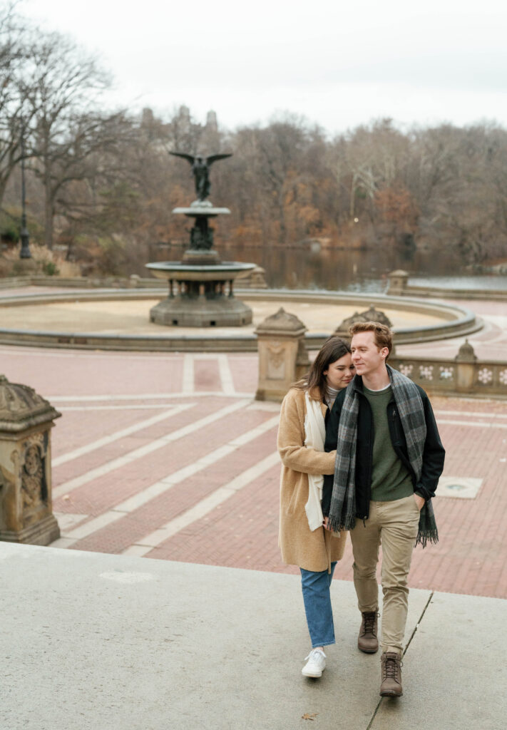 A couple walks together up the stairs at Bethesda Fountain in Central Park. Discover romantic photos from an engagement session in New York City.