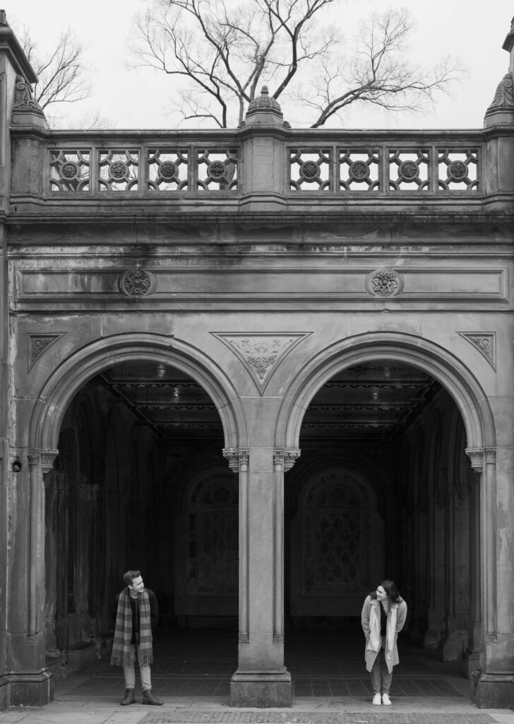 A couple stands together at The Arcade at Bethesda Terrace in Central Park. Discover documentary photos from an engagement session in New York City.