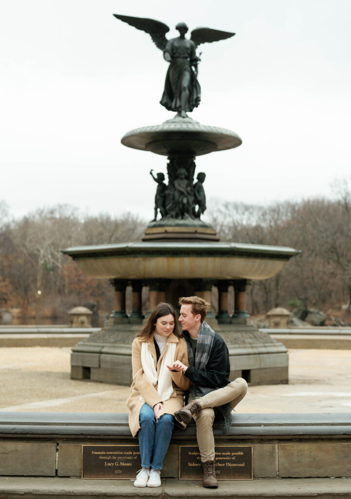 A couple sits together at Bethesda Fountain in Central Park. Discover romantic photos from an engagement session in New York City.