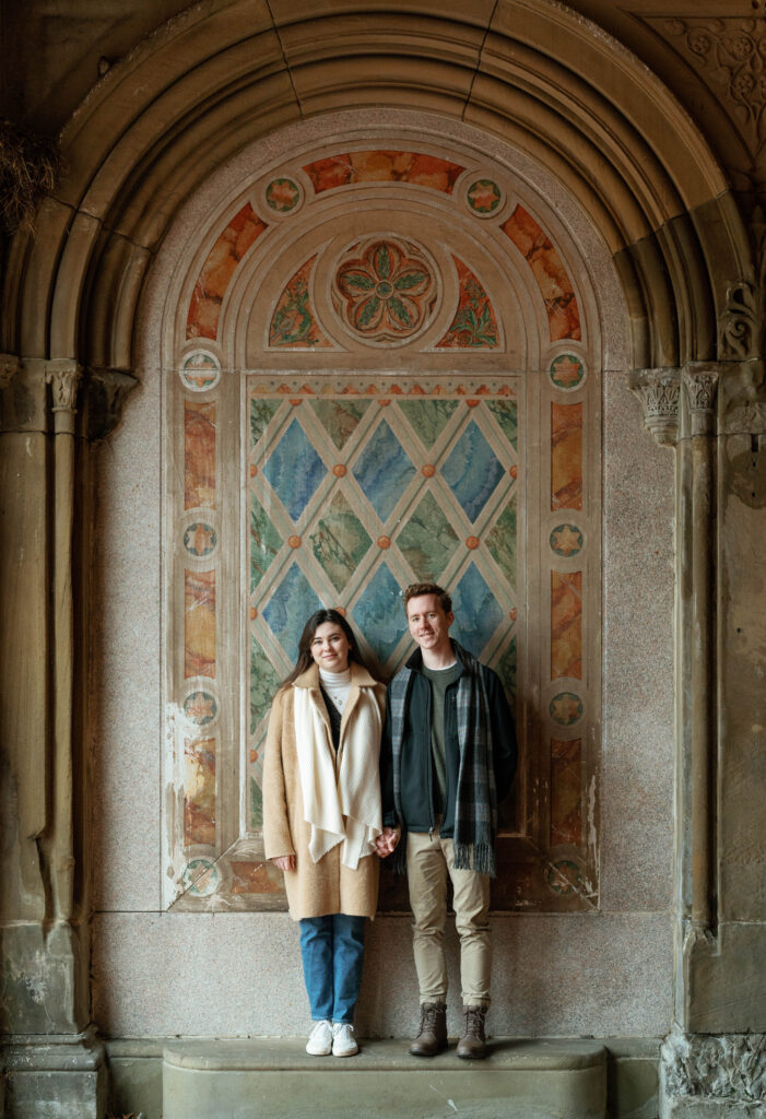 A couple stands together at The Arcade at Bethesda Terrace in Central Park. Discover documentary photos from an engagement session in New York City.