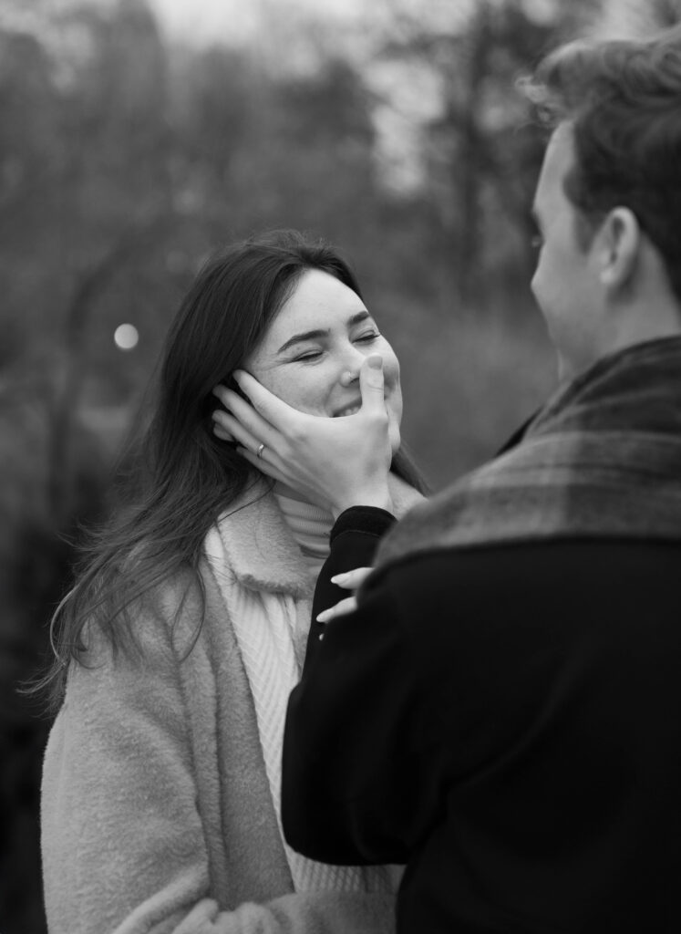 A couple has a candid moment together laughing as they walk around central park together in NYC to celebrate their engagement photos.