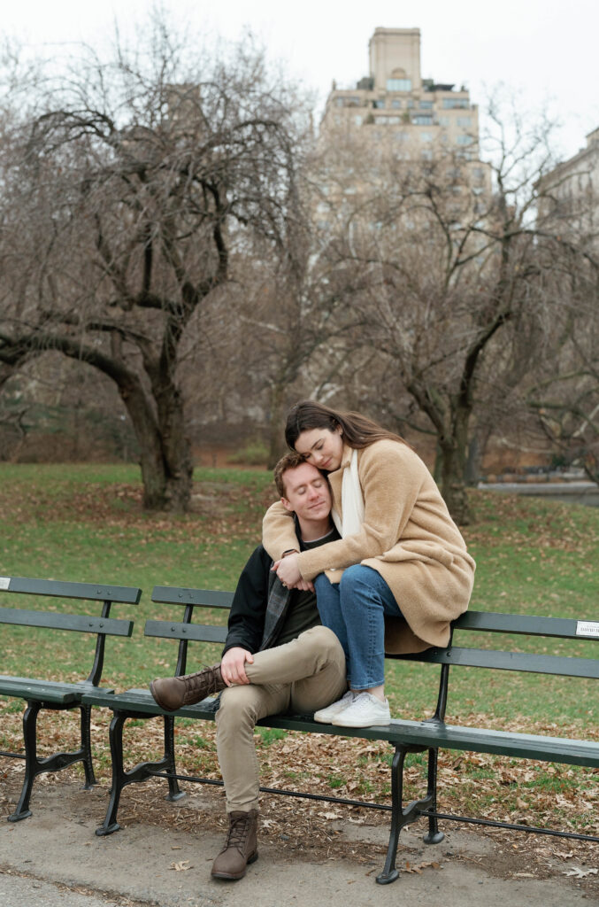 A couple sits together at a bench in Central Park. Discover candid engagement photography in New York City.  