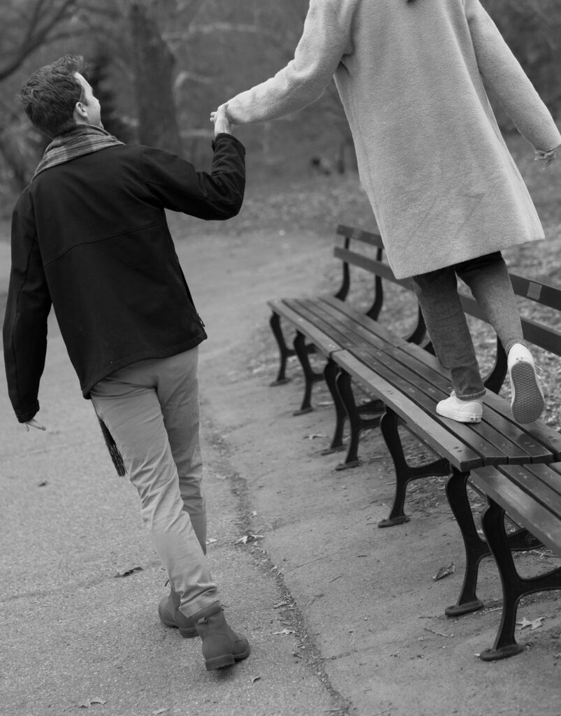 A couple walks together on a bench in Central Park. Discover candid engagement photography in New York City.  