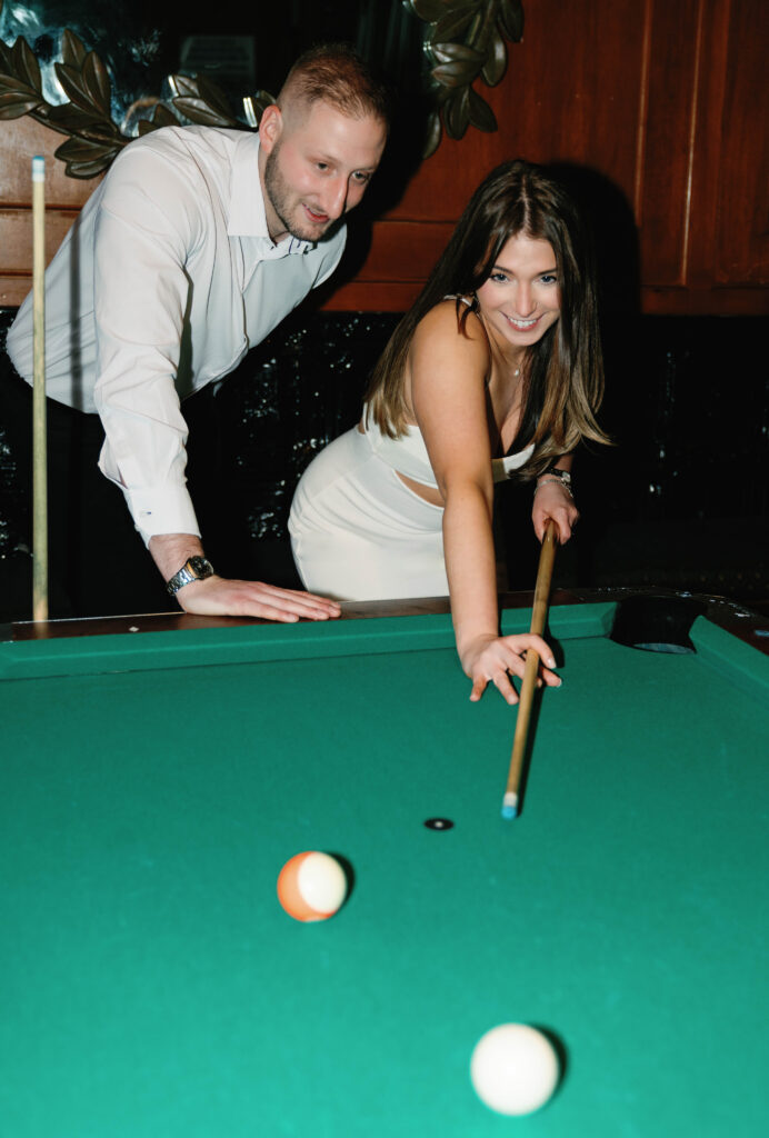 A candid photo of a couple playing pool at a bar to celebrate their love through documenting their engagement photos in New York City. 
