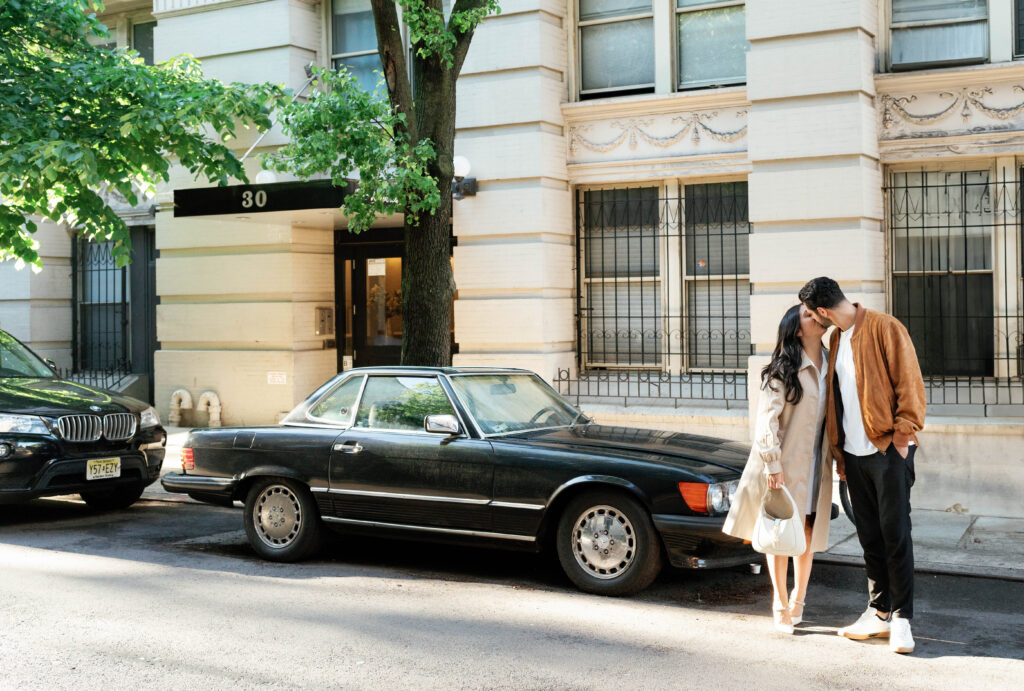 Engaged couple posing in front of a vintage car in the West Village in NYC. Discover documentary engagement photography in New York City. 