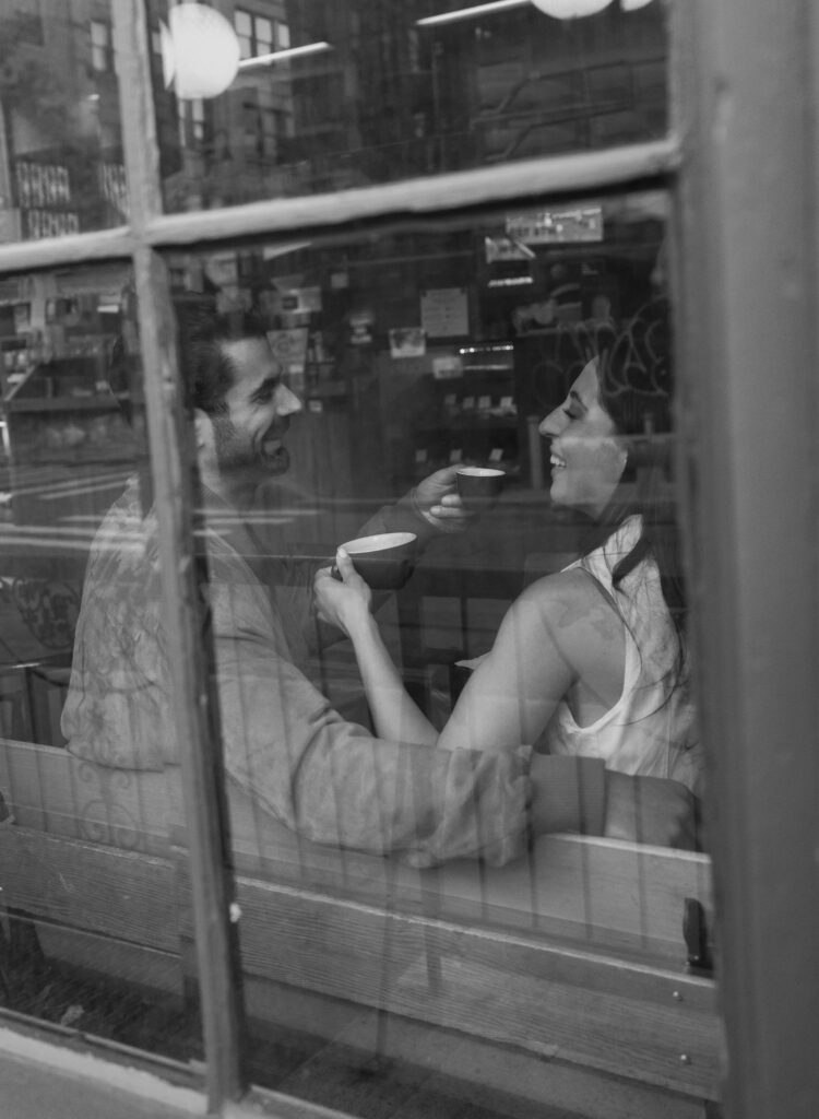 Candid moment of engaged couple laughing at a cozy West Village coffee shop in NYC. Discover documentary and editorial New York City engagement photos. 