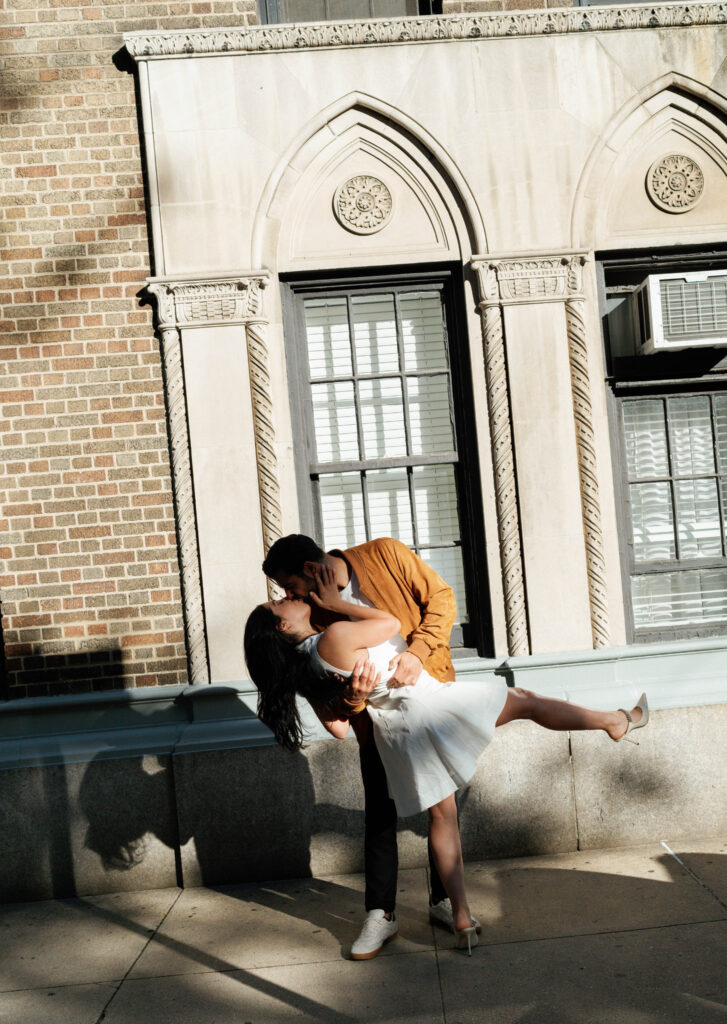 Romantic kiss between engaged couple in front of iconic Greenwich Village building. Discover intimate and documentary engagement photos in New York City. 