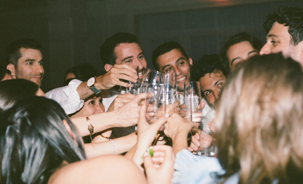 A candid photo of guests toasting their glasses at a reception. Discover destination documentary and editorial film wedding photography.